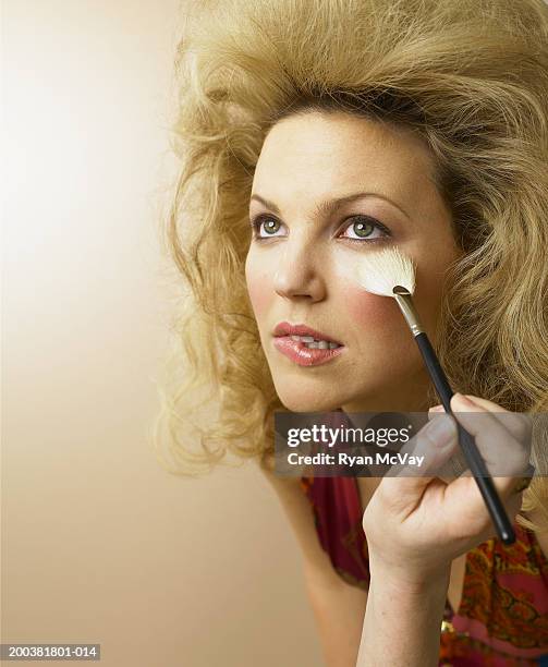 young female model biting lip as stylist applies make-up, looking up - pinceau à blush photos et images de collection