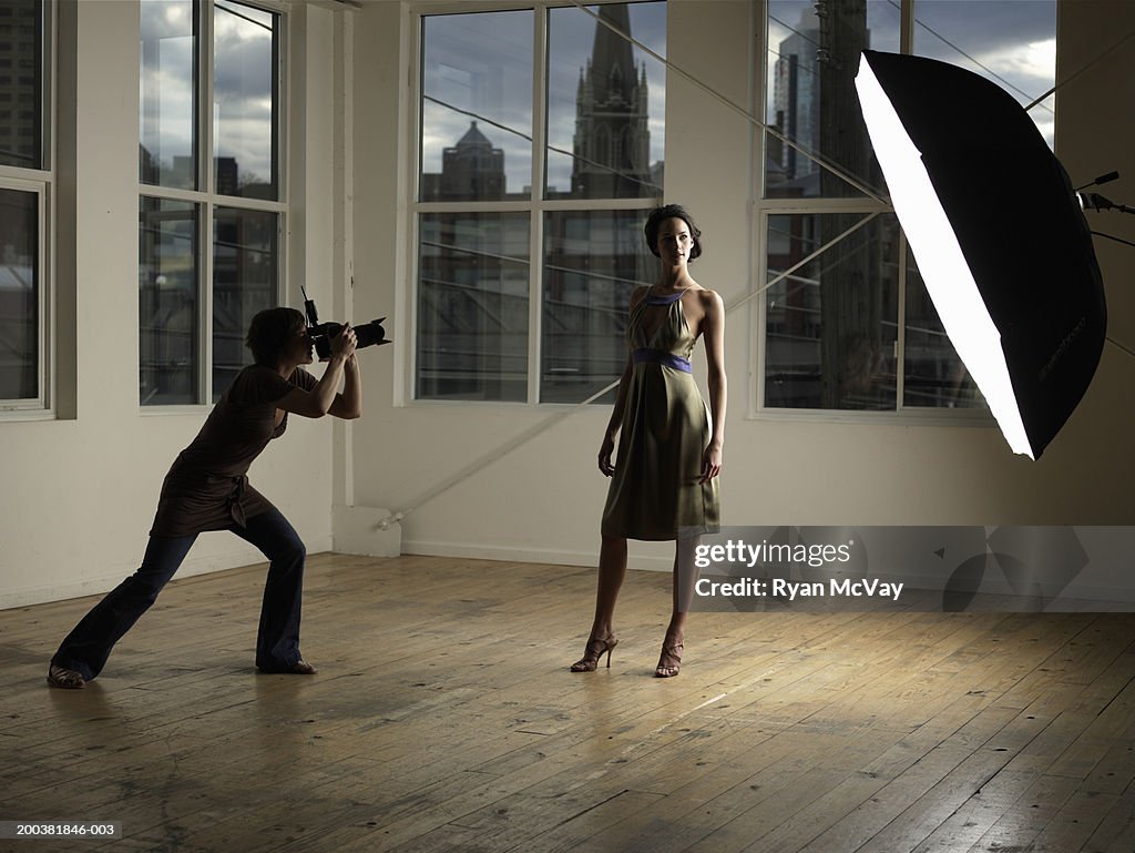 Woman photographing young female model in photo studio, dusk