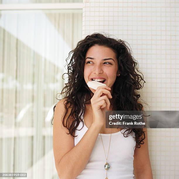 young woman eating ice lolly by tiled wall, looking away, smiling - woman looking through ice stock pictures, royalty-free photos & images