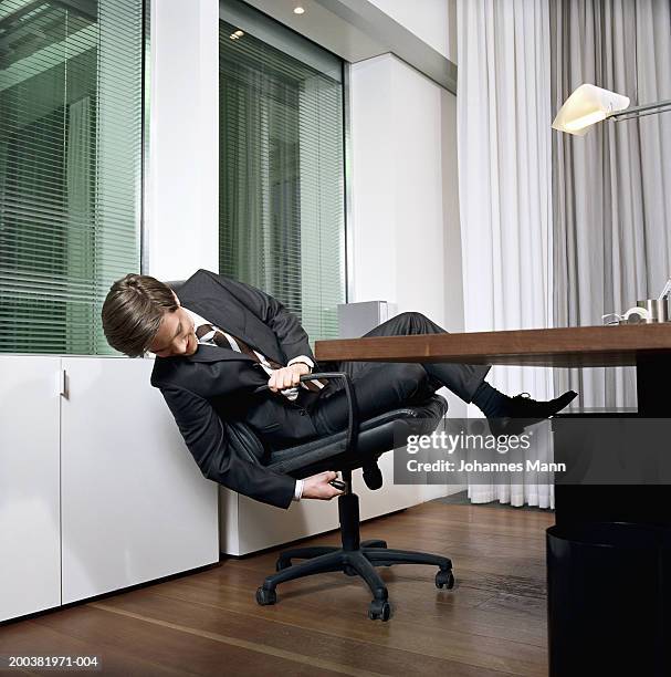 young businessman sitting at desk adjusting chair - adjusting stockfoto's en -beelden