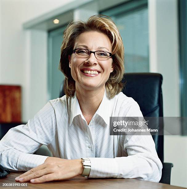 mature businesswoman sitting at desk, smiling, portrait - portrait mann business stock pictures, royalty-free photos & images