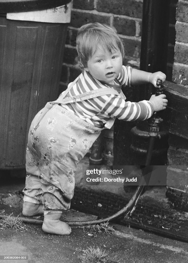 Boy (21-24 months) playing with garden tap, portrait (B&W)