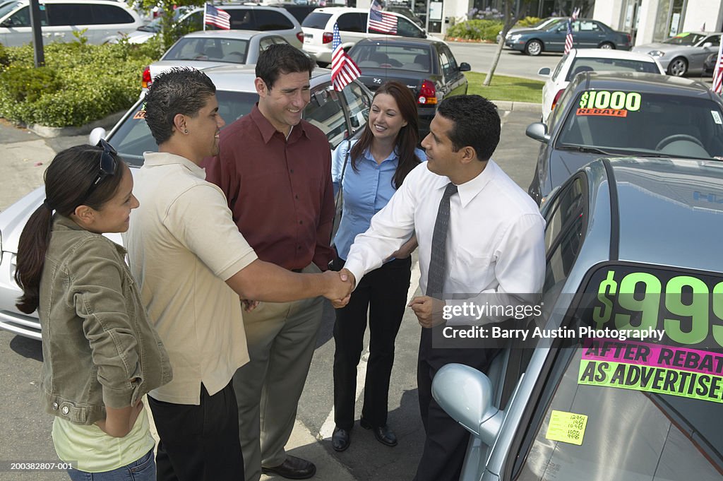Car salesman selling car to family, shaking young man's hand, smiling