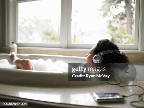 Young woman wearing headphones in bubble bath, smiling, side view Young woman wearing headphones in bubble bath, smiling, side view