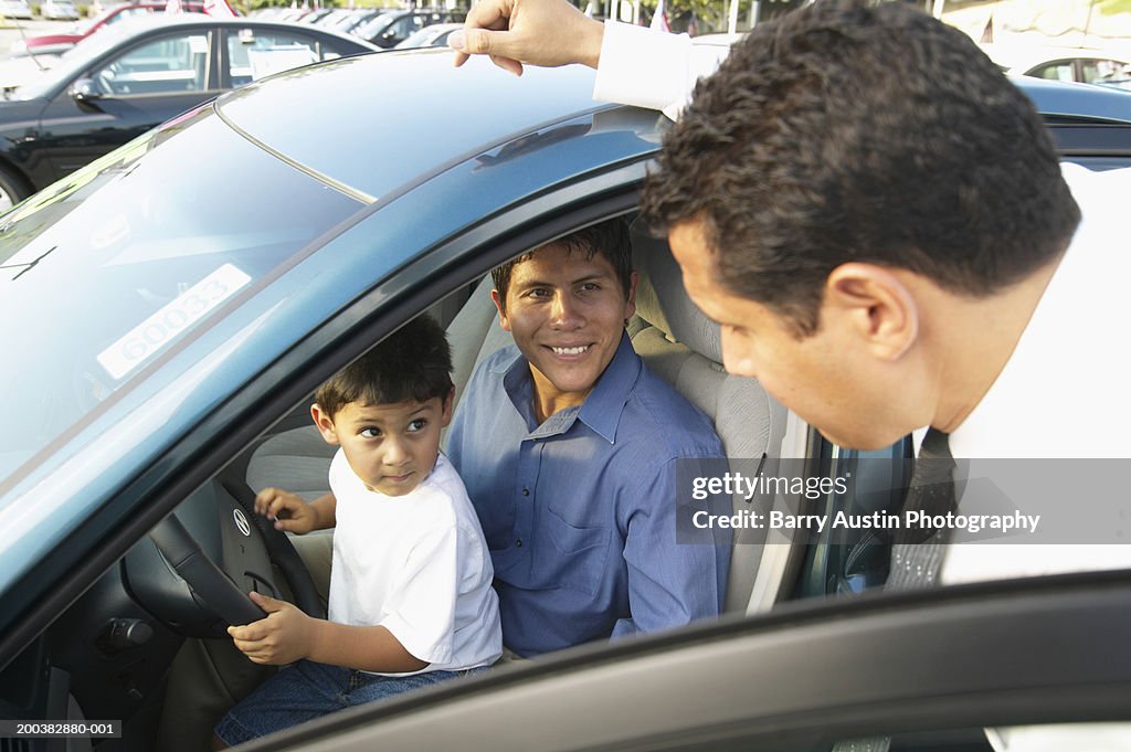 Man sitting in car with son (3-5) on lap, talking to car salesman