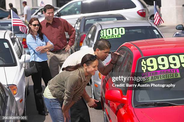 couple in car lot watching son and daughter (17-19) looking at car - auto sticker price stock pictures, royalty-free photos & images