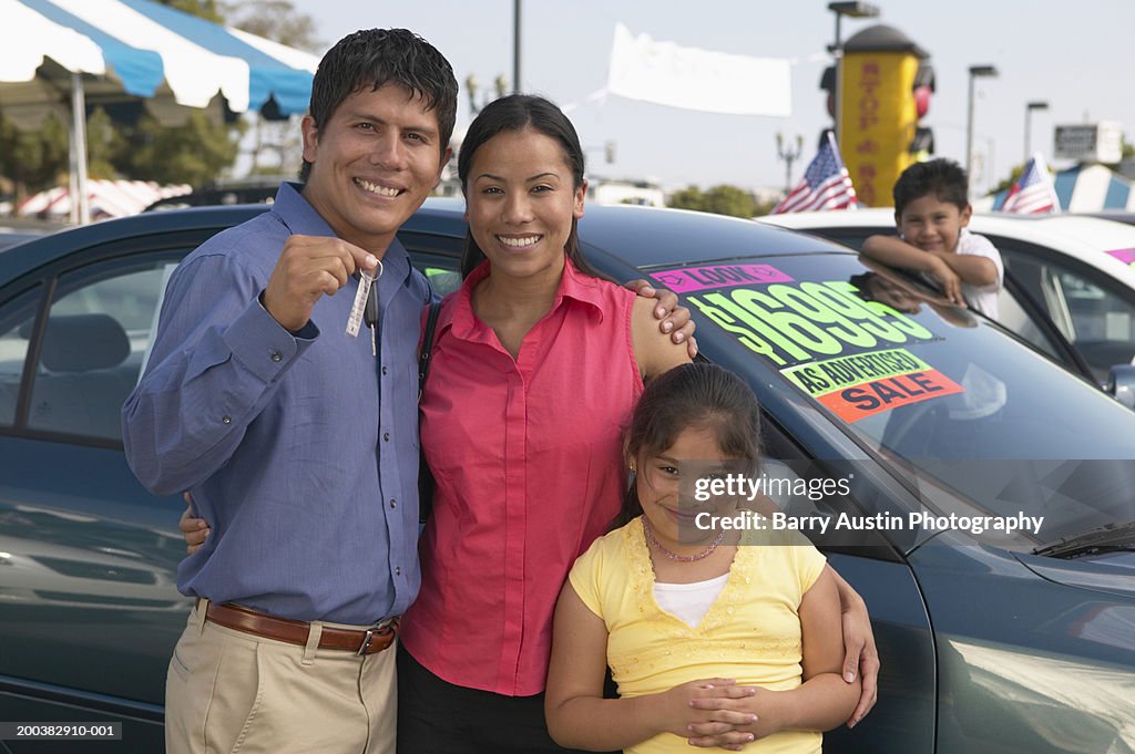 Family in car lot, father holding keys, smiling, portrait
