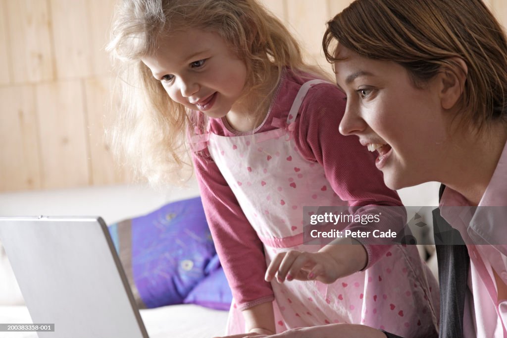 Mother and daughter (3-5) using laptop computer, smiling