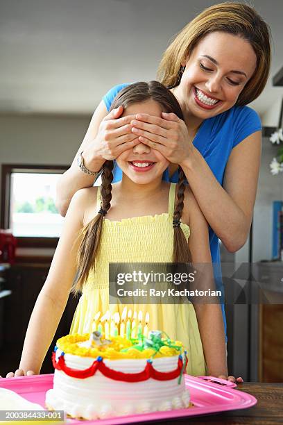 mother covering daughter's (10-12) eyes, birthday cake in foreground - girl 10 12 stock pictures, royalty-free photos & images