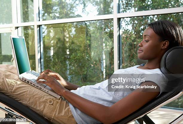 woman relaxing on futuristic reclining chair using laptop computer - recliner chair stock pictures, royalty-free photos & images