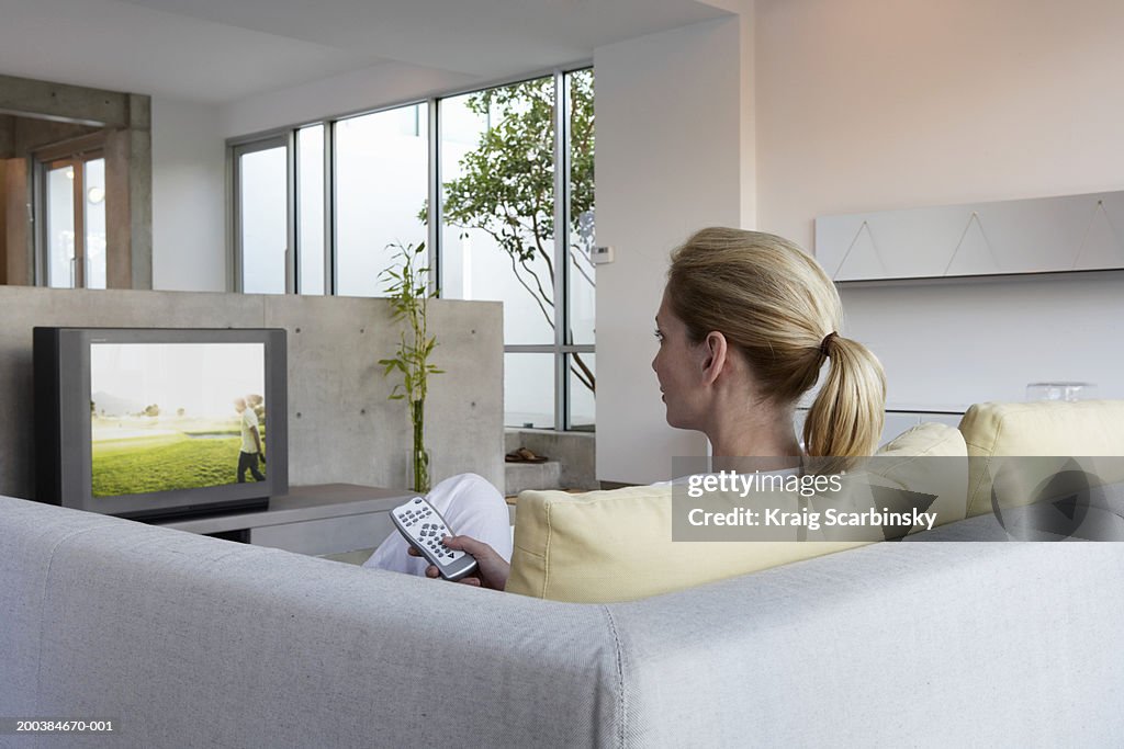 Woman relaxing on sofa watching television, rear view