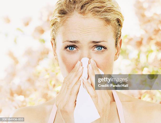 young woman blowing nose on tissue, close up, portrait - allergie stockfoto's en -beelden