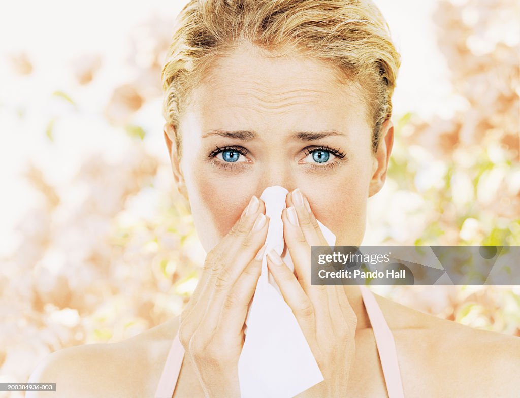 Young woman blowing nose on tissue, close up, portrait