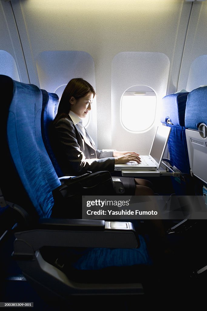 Young businesswoman working on laptop, sitting in airplane, side view