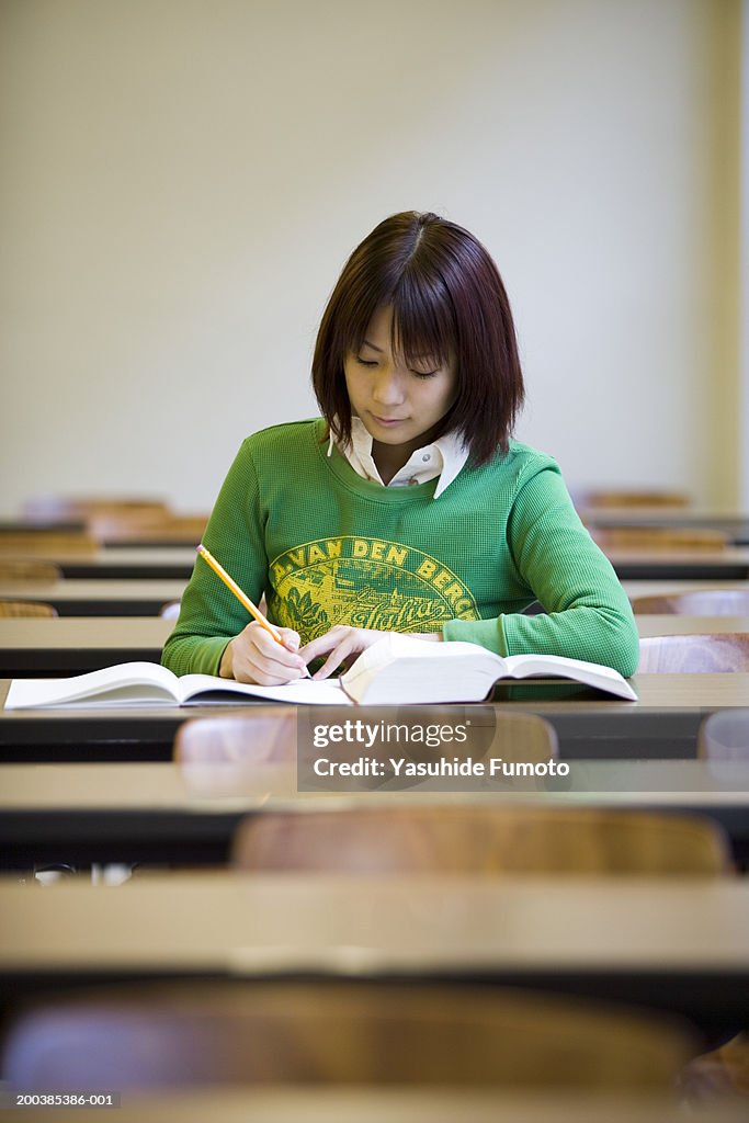 Young woman sitting in classroom, writing