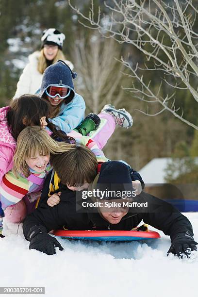 father and four children (7-10) piled on sled in snow, laughing - familie mit vier kindern stock-fotos und bilder