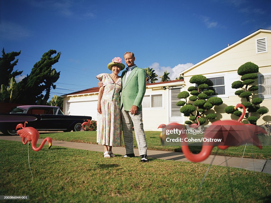 Senior couple in front of their home with toy flamingoes