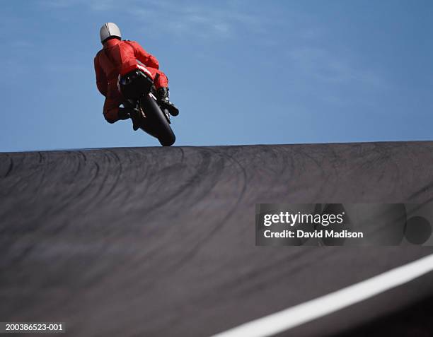 motorcycle racer cresting hill, rear view, low angle view - route moto stock-fotos und bilder