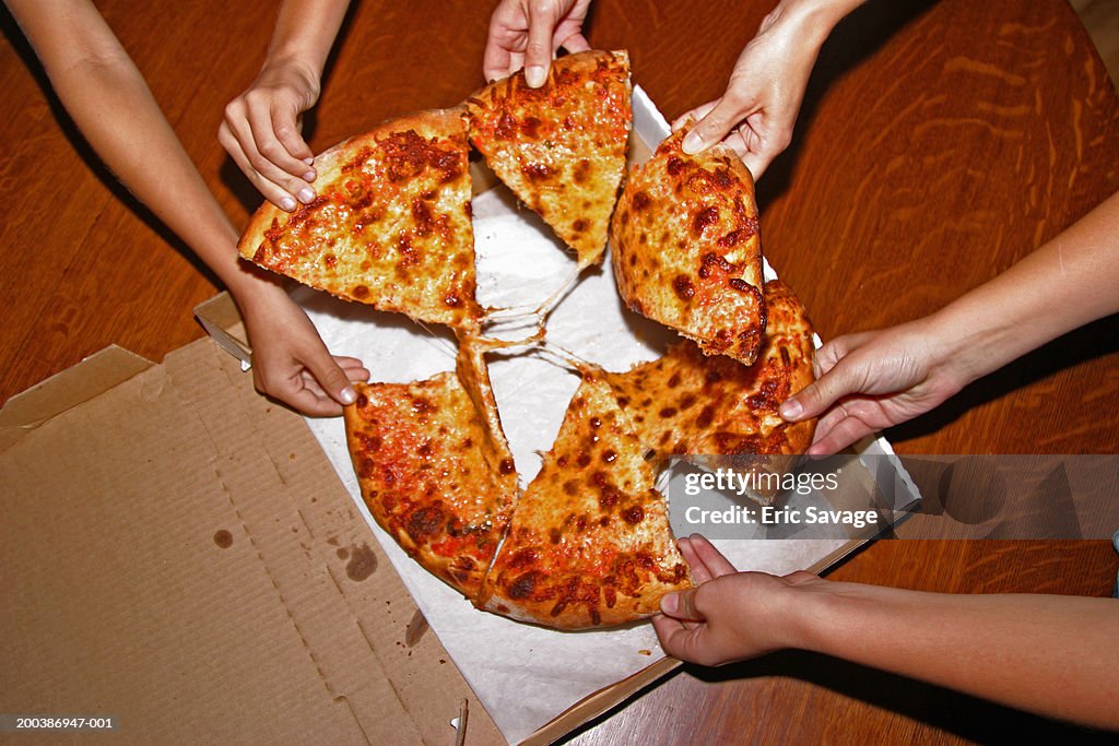 People grabbing slices of pizza, overhead view