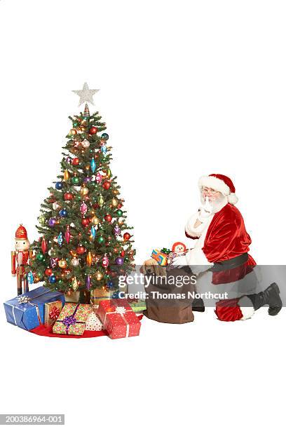 santa claus kneeling beside christmas tree, finger on lips, side view - man with tape on lips stock pictures, royalty-free photos & images