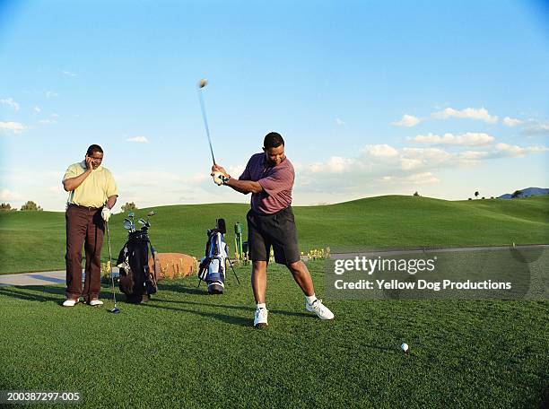 golfer driving ball, other golfer on mobile phone (blurred motion) - swing de golf bildbanksfoton och bilder