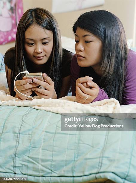 teenage girls (13-16) looking at mp3 player, lying on bed - next to stock pictures, royalty-free photos & images