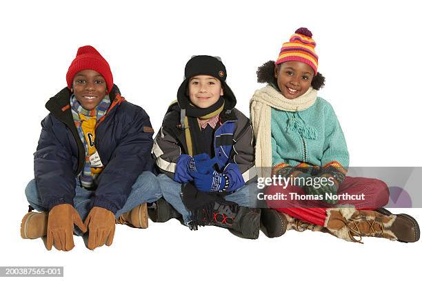 three children (8-10) in winter clothing sitting side by side, smiling - winter coat fotografías e imágenes de stock