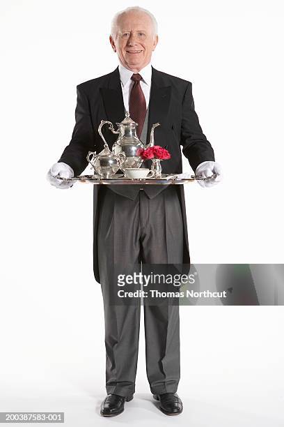 senior male butler carrying teapot on serving tray, smiling, portrait - buttler stock-fotos und bilder