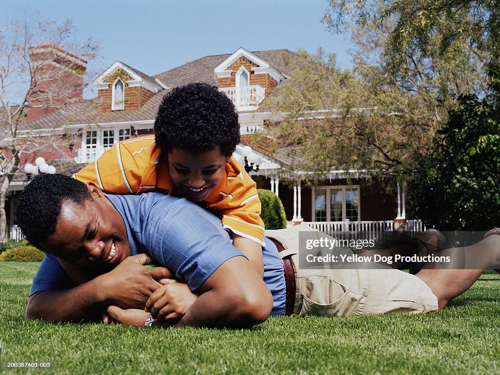 Father and son (10-12) wrestling for football on lawn