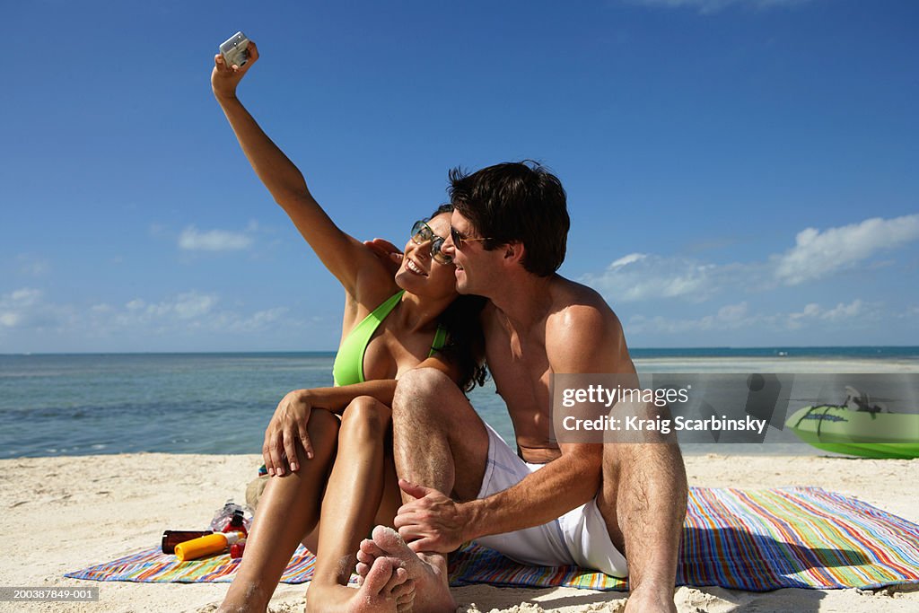 Couple on beach blanket taking picture, smiling