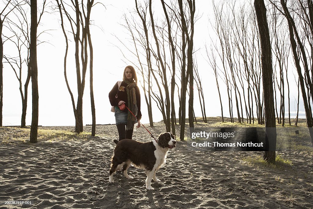 Teenage girl (15-17) walking English springer spaniel on beach, spring