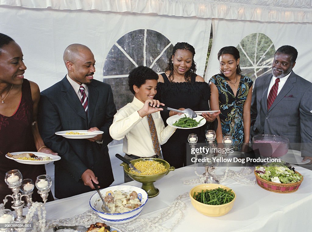 Family watching boy (10-12) filling plate with green beans at party