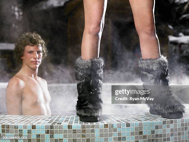 woman in furry boots standing on edge of hot tub, young man in hot tub - botas de après ski fotografías e imágenes de stock