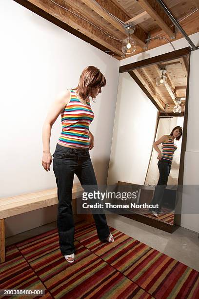 young woman trying on clothing in dressing room, looking in mirror - full length mirror stock-fotos und bilder