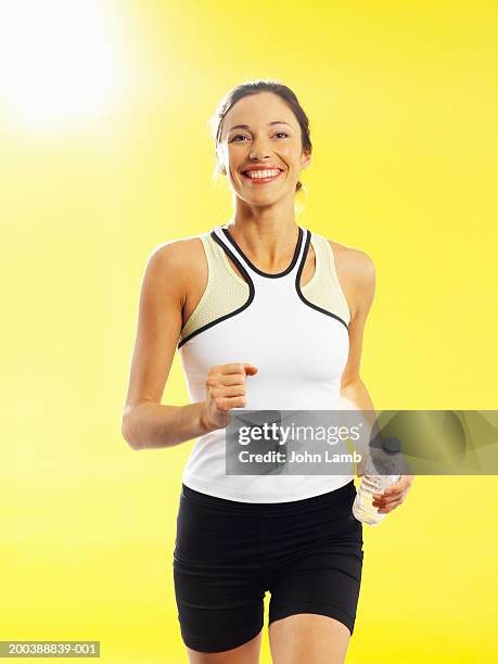young woman running along with bottled water, smiling, portrait - running shorts foto e immagini stock