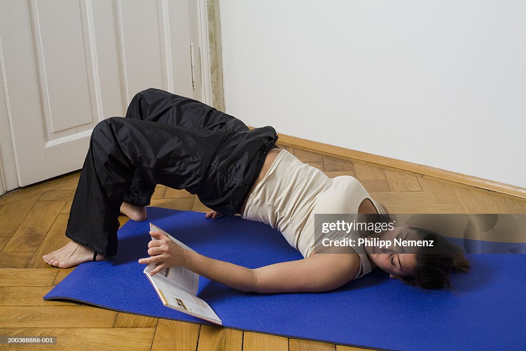 Young woman lying on mat performing exercises from book