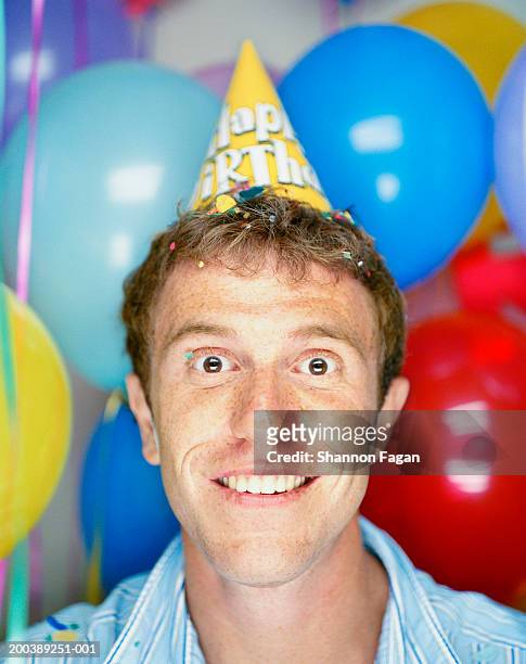 young man wearing birthday party hat, smiling, close-up - birthday hat stock pictures, royalty-free photos & images