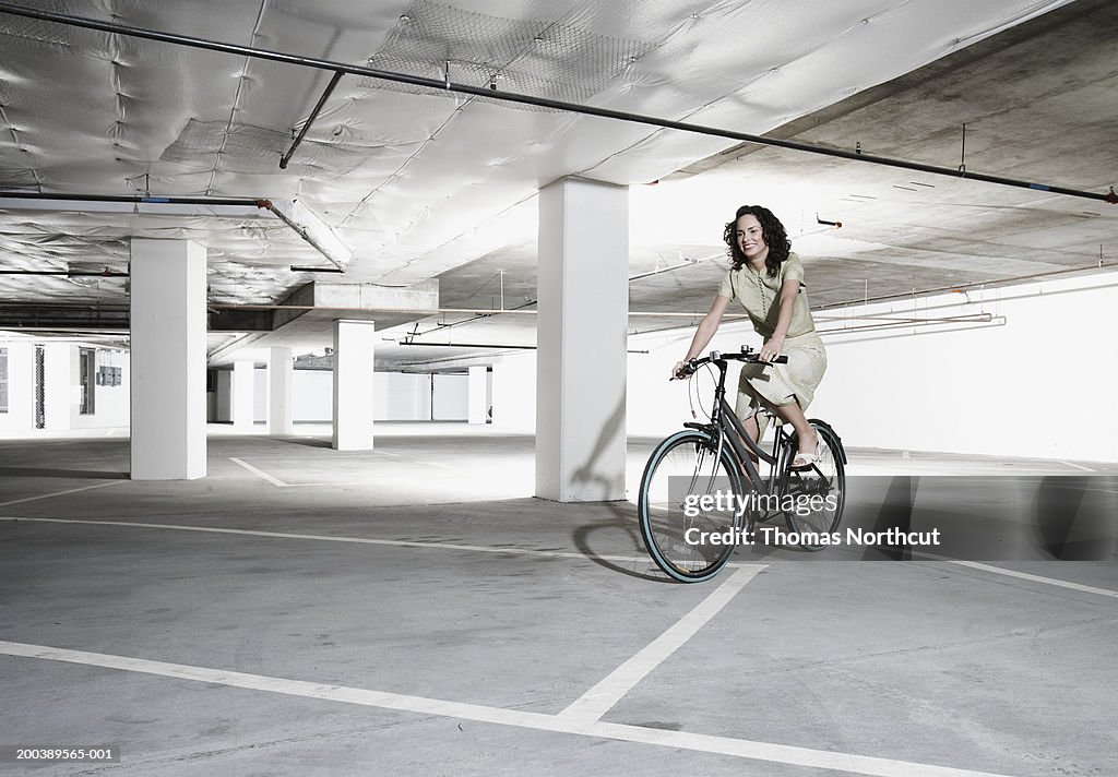 Young woman riding bicycle in parking garage, smiling