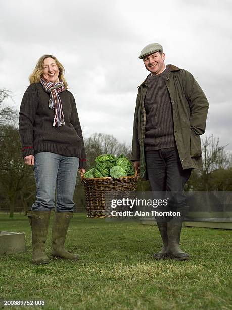 couple standing in field holding basket of cabbages, smiling, portrait - couple farm stock pictures, royalty-free photos & images