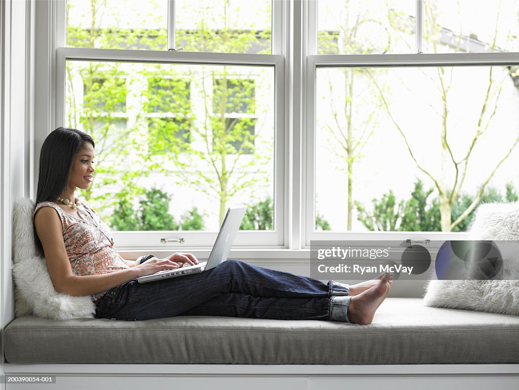 Teenage girl (15-17) using laptop on window seat, side view