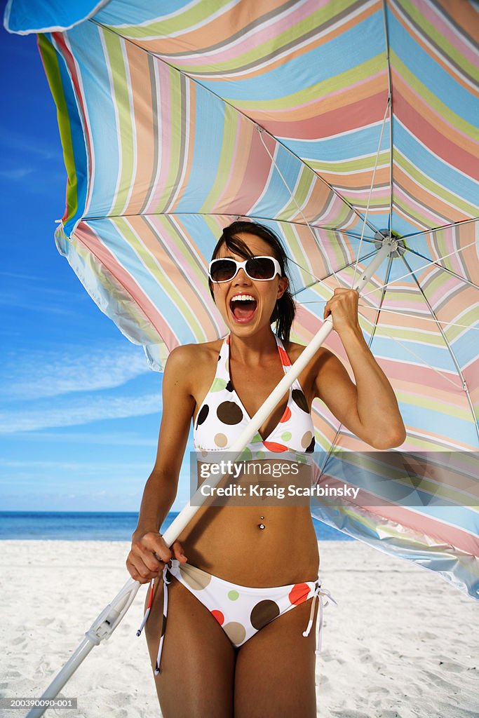 Young woman holding beach umbrella, smiling, portrait, close-up