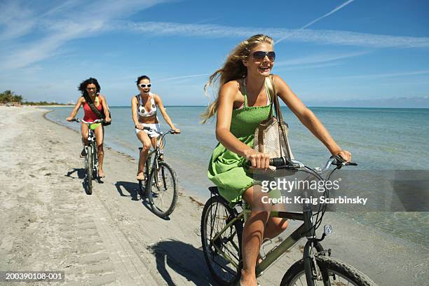 three young women riding bicycles on beach, smiling - beach fun stock pictures, royalty-free photos & images