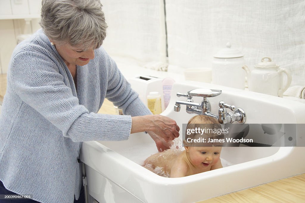 Grandmother bathing baby granddaughter (8-10 months) in sink, smiling
