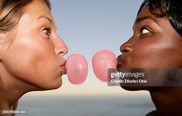 two young women face to face blowing bubble gum, profile, close-up - kauwgom stockfoto's en -beelden