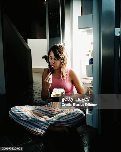 young woman sitting by open refrigerator, eating ice cream - evening indulgence stock pictures, royalty-free photos & images