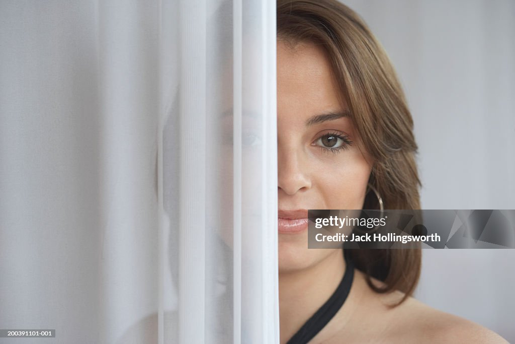 Portrait of a young woman hiding behind a curtain