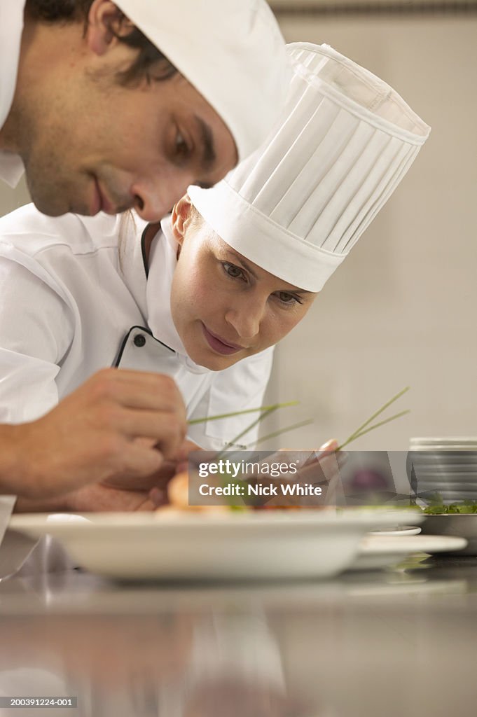 Female chef and male cook adding garnish to dishes, low angle view