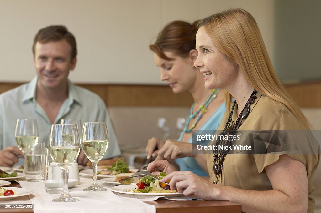 Woman having meal in restaurant with friends, smiling, side view