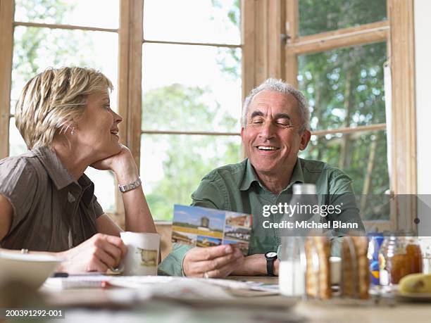 mature couple at breakfast table, man holding postcard, smiling - postcards stock pictures, royalty-free photos & images