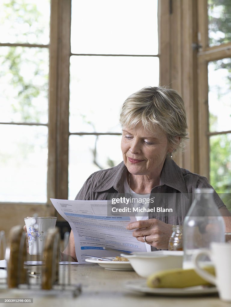 Mature woman sitting at breakfast table reading letter